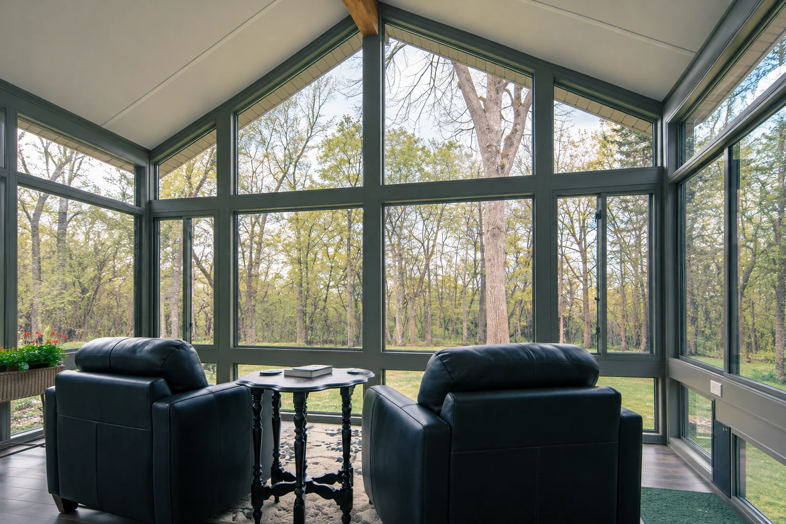 Custom sunroom interior with dark-framed floor-to-ceiling windows, two leather chairs and a wooded view.