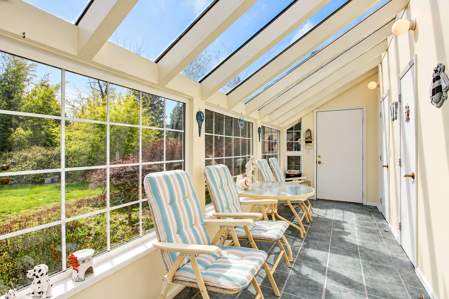 Solarium with a glass-paneled roof, large windows, tiled floor and striped lounge chairs.